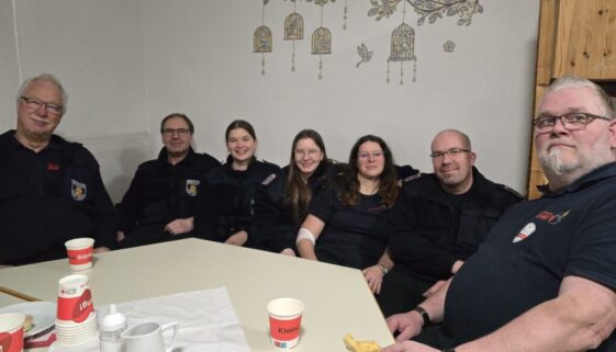 8 Feuerwehrmitglieder sitzen auf Bank in gemütlicher Runde, nach erfolgter Blutspende