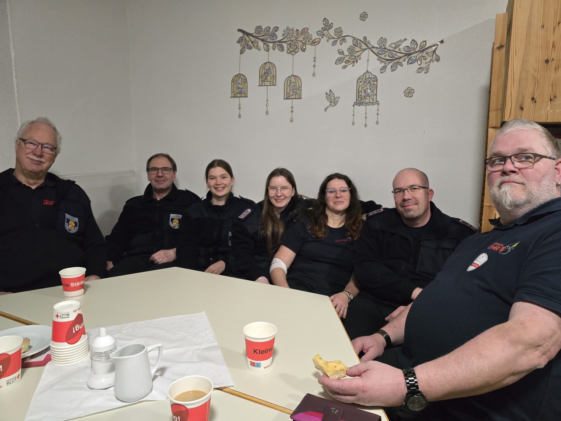 8 Feuerwehrmitglieder sitzen auf Bank in gemütlicher Runde, nach erfolgter Blutspende